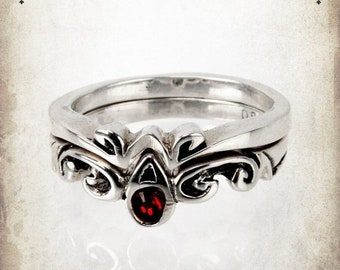 May include: A silver ring with a red gemstone set in a decorative design. The ring is a double band with a filigree pattern.