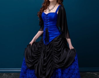 May include: A woman wearing a blue corset with black lace-up detailing and a black and blue layered skirt. She is wearing a white flower in her hair and a silver necklace. The background is a dark blue wall with ornate white floral designs in the corners.