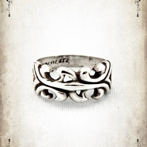 Puede incluir: Anillo de plata con un dise&ntilde;o decorativo y ornamentado. El anillo est&aacute; grabado con la palabra "Dracolite".