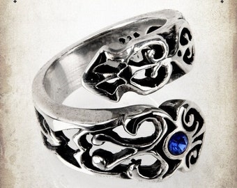May include: A silver ring with an intricate design and a blue gemstone. The ring is open on one side and has a twisted design.