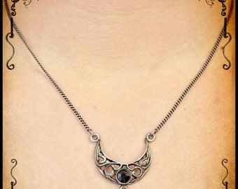 Puede incluir: Un collar de plata en forma de media luna con un colgante de piedra preciosa negra. El colgante tiene un diseño detallado y cuelga de una cadena delicada.