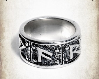 May include: A silver ring with a textured band and raised runes. The runes are in a rectangular shape and are surrounded by small dots.