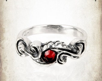 May include: A silver ring with a red gemstone set in a swirling, ornate design. The ring is made of sterling silver and features a red gemstone.