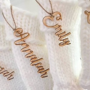 May include: Four white knitted stockings with wooden name tags. The names on the tags are "Annabelle", "Emily", "Ava", and "Lisa".