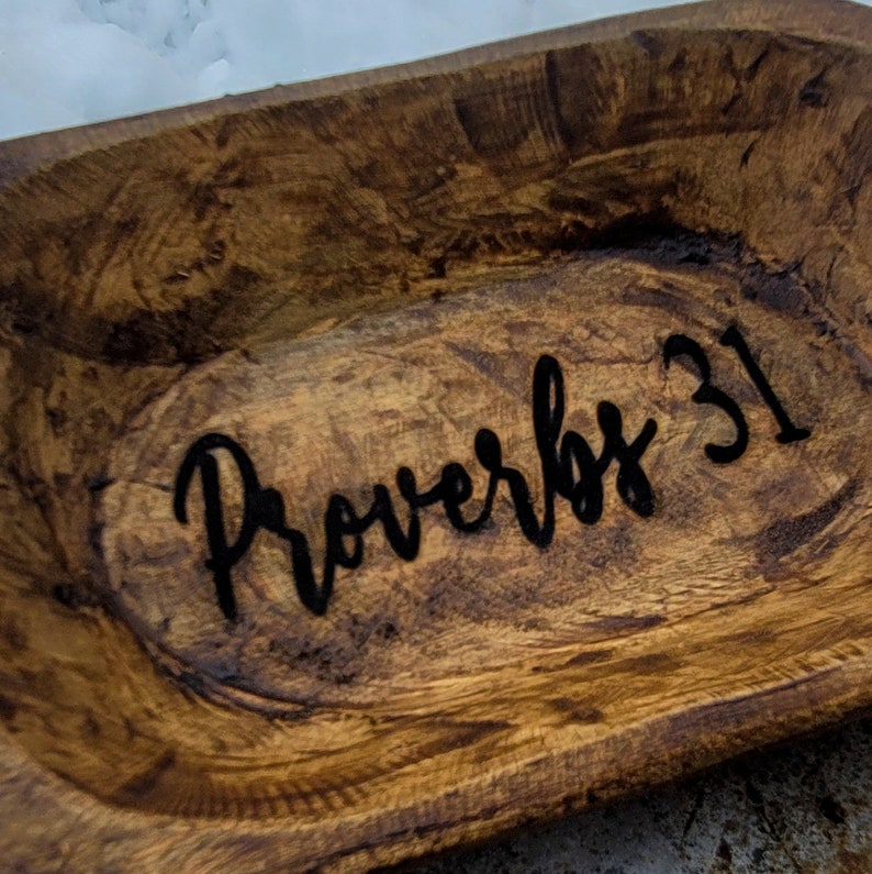 May include: A wooden dough bowl with a dark brown stain. The words "Proverbs 31" are engraved in black lettering on the inside of the bowl.