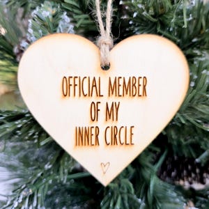 May include: A heart-shaped wooden ornament with the text "OFFICIAL MEMBER OF MY INNER CIRCLE" burned into the wood. A small heart is etched at the bottom. The ornament hangs from a natural twine string.