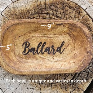 May include: A wooden bowl with a rustic finish, measuring approximately 9 inches long and 5 inches wide. The bowl is engraved with the word "Ballard".
