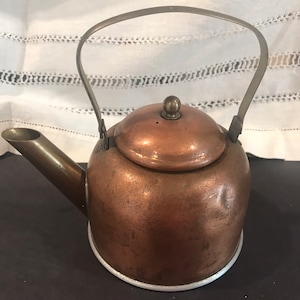 May include: A vintage copper teapot with a silver handle and a silver lid. The teapot has a worn, aged look.