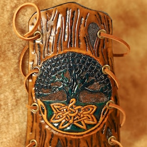 Könnte beinhalten: Ein brauner Lederarmreif mit einem Lebensbaum-Design. Der Armreif hat einen detaillierten geprägten Baum mit einem keltischen Knoten und wird mit Lederschnürung befestigt. Der Armreif ist etwa 18 cm hoch.