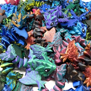 May include: A collection of iridescent, miniature dragon figurines in various colors, including green, blue, purple, and red. The dragons are made of a shiny, metallic material and have intricate details.