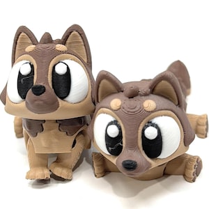 May include: Two 3D-printed dog figurines. One stands upright, the other is lying down. Both have large, expressive eyes with black pupils and white highlights. The dogs are primarily brown and tan, with textured details and a cartoonish design.