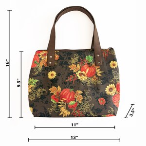 May include: A brown tote bag with a fall-themed floral pattern featuring pumpkins and sunflowers. The bag is 16 inches tall, 11 inches wide, and 3.5 inches deep. It has brown handles and measures 13 inches across the bottom.