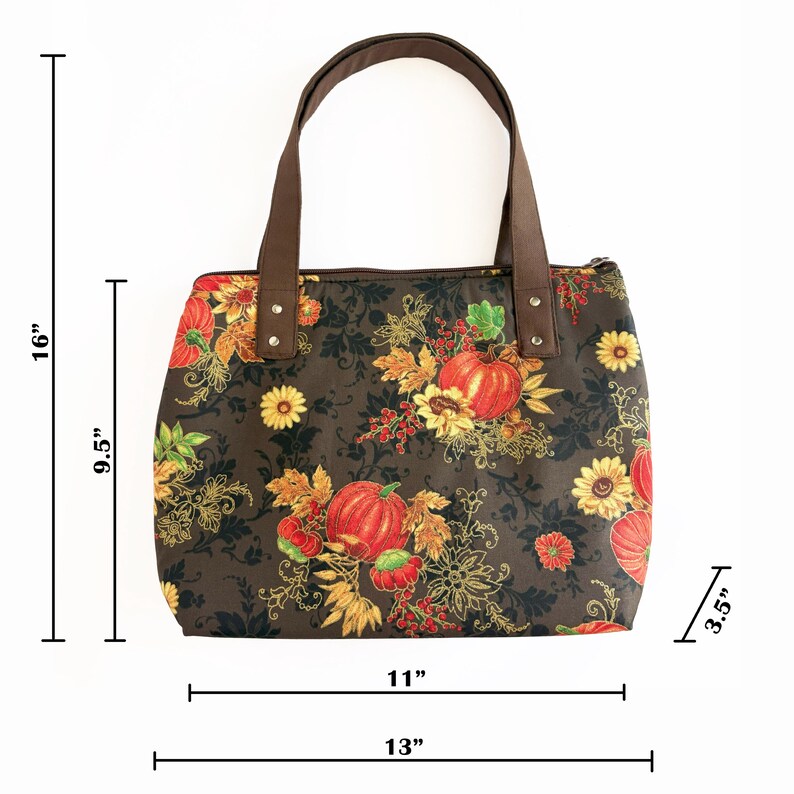 May include: A brown tote bag with a fall-themed floral pattern featuring pumpkins and sunflowers. The bag is 16 inches tall, 11 inches wide, and 3.5 inches deep. It has brown handles and measures 13 inches across the bottom.