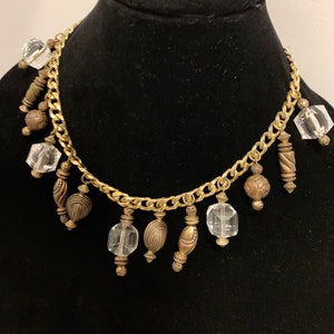 May include: A gold chain necklace with multiple clear glass and brown metal beads hanging from it.