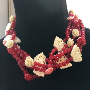 May include: A multi-strand necklace with red and white beads and carved white flower and butterfly charms.