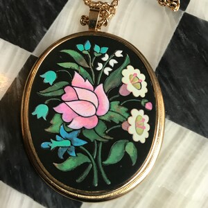 May include: A gold chain necklace with an oval pendant featuring a black background and a colorful floral design. The pendant has a pink rose, white flowers, blue flowers, and green leaves.