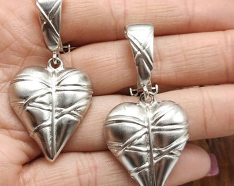 May include: A pair of silver heart-shaped earrings with a textured, woven design. The earrings have a simple, elegant style.
