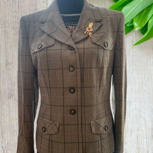 Puede incluir: Una chaqueta de cuadros marrón y negro con cierre de botones y dos bolsillos de solapa. La chaqueta tiene una silueta ajustada y se lleva en un maniquí.