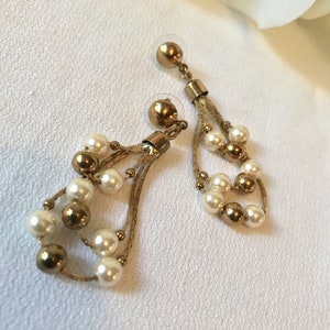 May include: A pair of gold tone dangle earrings with multiple strands of chain and white faux pearls.
