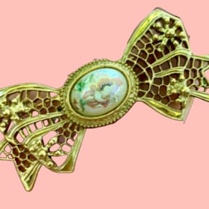 May include: A gold-toned metal bow brooch with a white cameo featuring a floral design.