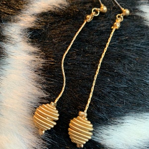May include: A pair of gold dangle earrings with a long chain and a coiled oval-shaped charm at the bottom.
