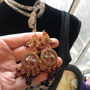 May include: Gold earrings with red and white stones, featuring a floral design and dangling red beads.