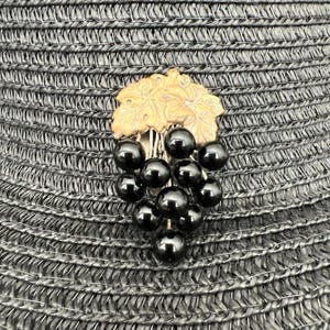 May include: A black and gold grape cluster brooch with a detailed floral design. The brooch is made of metal and has a cluster of black beads that resemble grapes.