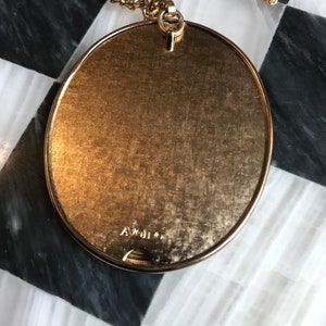 May include: A gold-tone oval pendant necklace with a chain. The back of the pendant has the inscription "A. Weil Co."