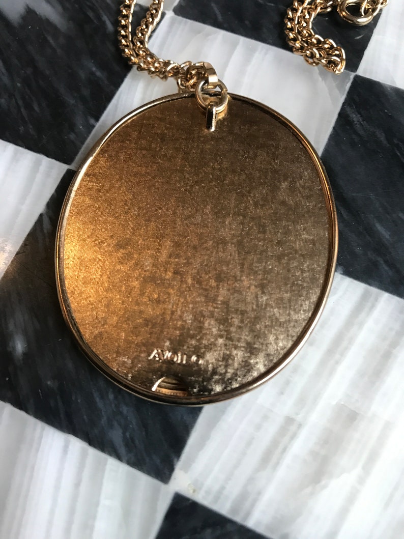 May include: A gold-tone oval pendant necklace with a chain. The back of the pendant has the inscription "A. Weil Co."