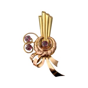 May include: A gold and rose gold tone brooch with a cluster of three pink stones and a bow design.