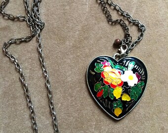 May include: A silver chain necklace with a black heart-shaped pendant. The pendant is decorated with colorful enamel flowers and leaves.