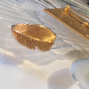 May include: A gold-toned feather-shaped brooch with a pin on the back.