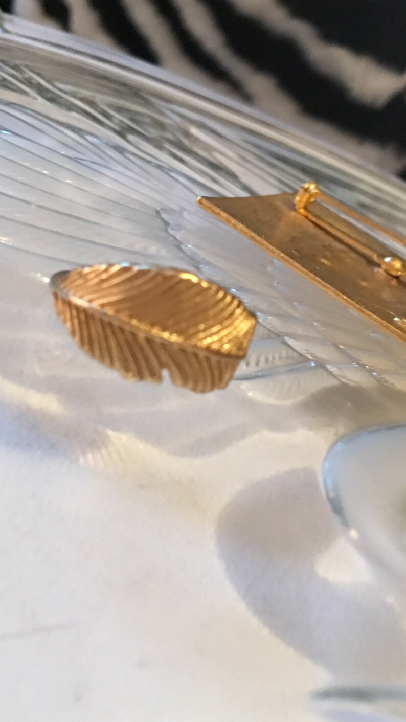 May include: A gold-toned feather-shaped brooch with a pin on the back.