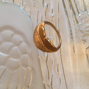 May include: A gold ring with a feather design. The ring is on a white background.