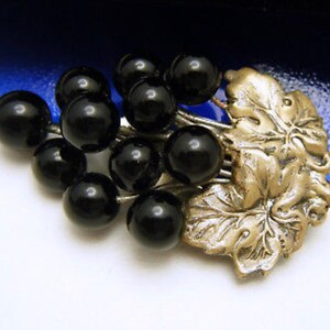 May include: A silver grapevine brooch with black glass grapes. The brooch is detailed with leaves and vines.