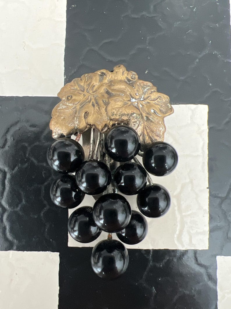 May include: A vintage brooch featuring a cluster of black glass grapes hanging from a gold-toned metal vine.