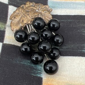 May include: A vintage brooch featuring a cluster of black glass grapes hanging from a gold-toned leaf.