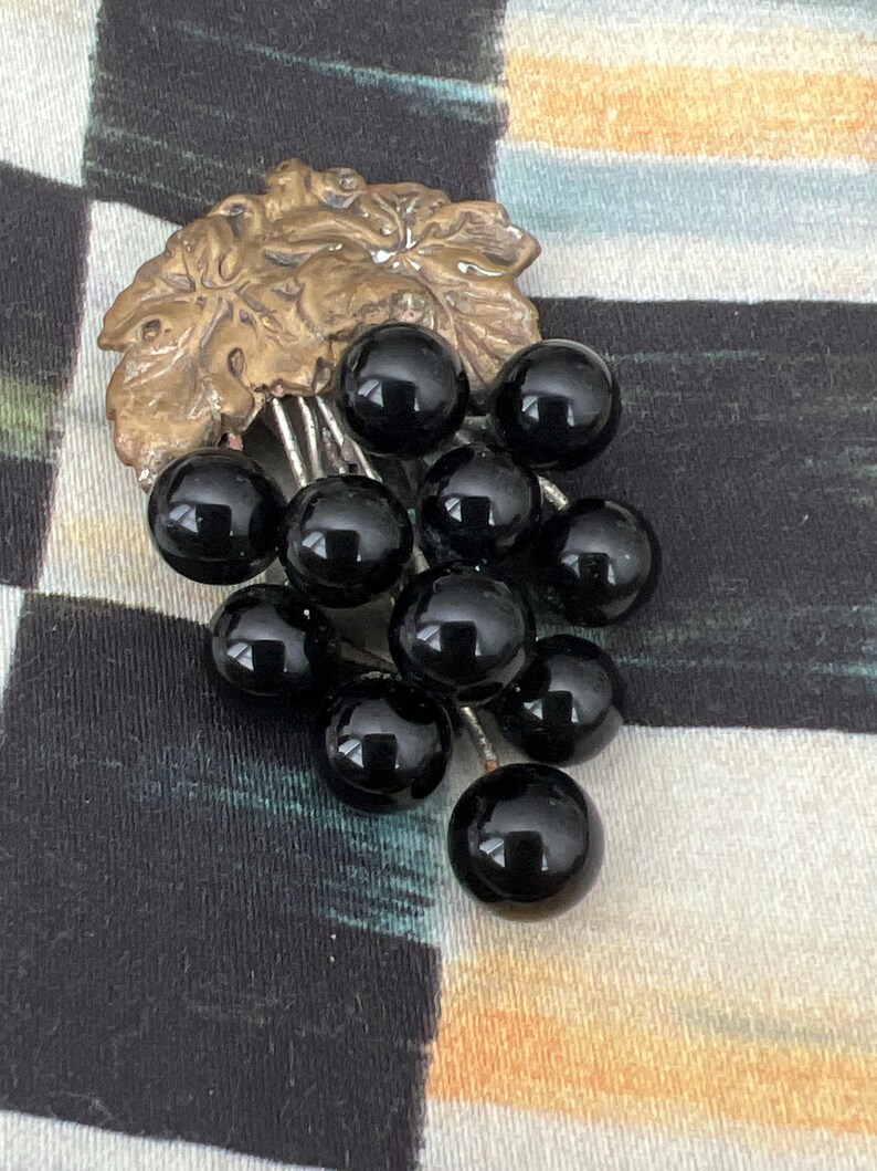 May include: A vintage brooch featuring a cluster of black glass grapes hanging from a gold-toned leaf.