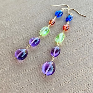 May include: A pair of long, dangling earrings with a rainbow of colors. The earrings feature a series of oval-shaped beads in shades of blue, green, orange, and purple, connected by gold wire.
