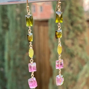 May include: Gold earrings with a graduated chain of green, yellow, and pink gemstones. The gemstones are rectangular and faceted.