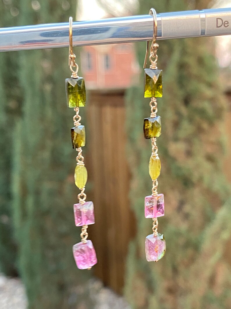May include: Gold earrings with a graduated chain of green, yellow, and pink gemstones. The gemstones are rectangular and faceted.