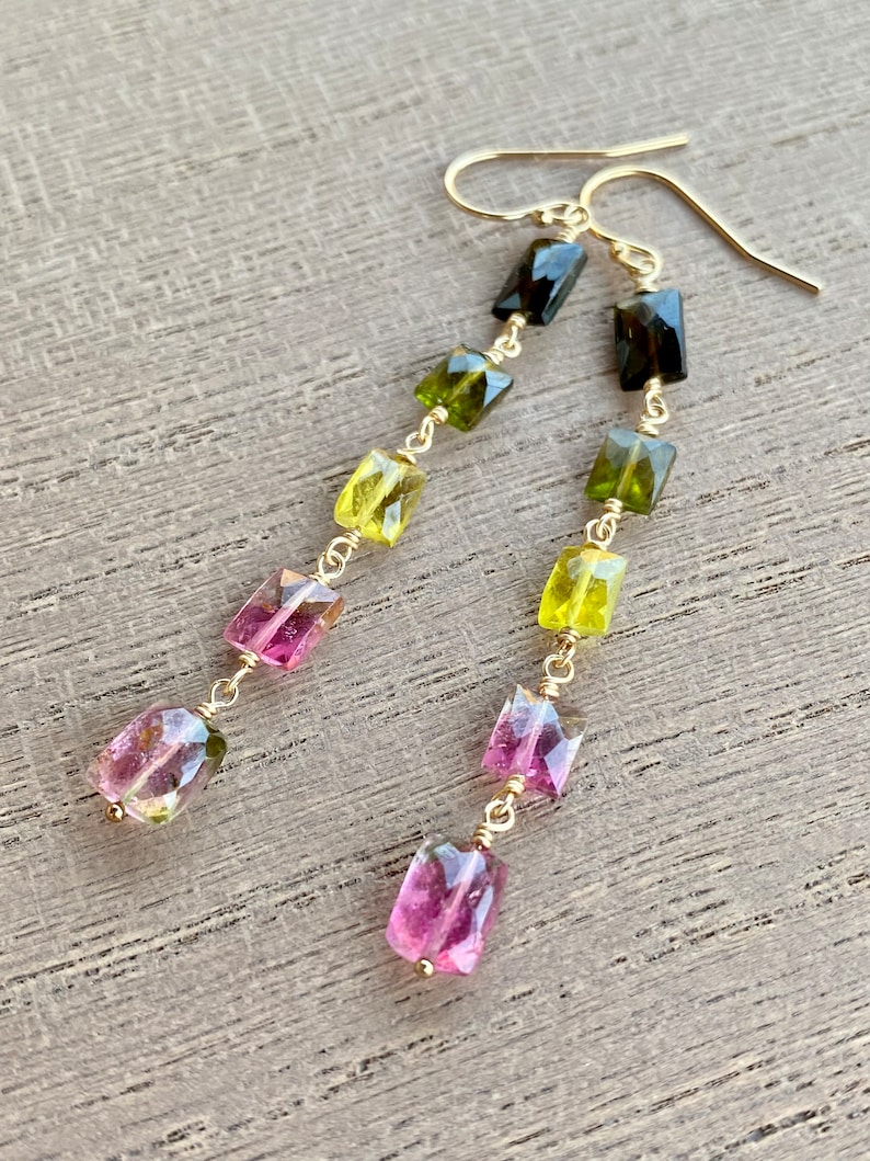 May include: Gold earrings with a cascading design of green, pink, and yellow gemstones. The gemstones are faceted and have a rectangular shape.