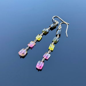 May include: A pair of long silver earrings with green, pink, and yellow gemstone beads.