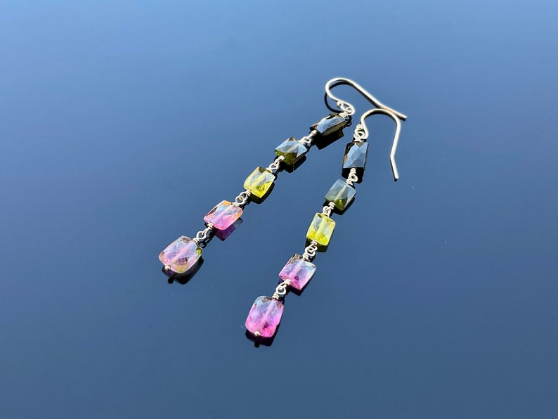 May include: A pair of long silver earrings with green, pink, and yellow gemstone beads.