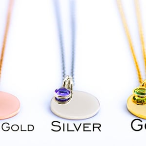 May include: Three pendant necklaces in rose gold, silver, and gold. Each necklace features a round pendant with a gemstone accent. The rose gold pendant has a red gemstone, the silver has a purple gemstone, and the gold has a green gemstone. The text "ROSE GOLD", "SILVER", and "GOLD" are below each necklace.