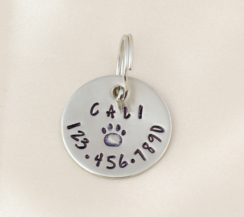 Silver Dog tag hand stamped with pet name, symbol and Phone number.