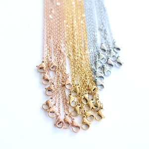 May include: An assortment of delicate chain necklaces in rose gold, gold, and silver tones. Each chain features a lobster clasp closure. The necklaces are displayed against a white background, showcasing their varying metallic finishes.