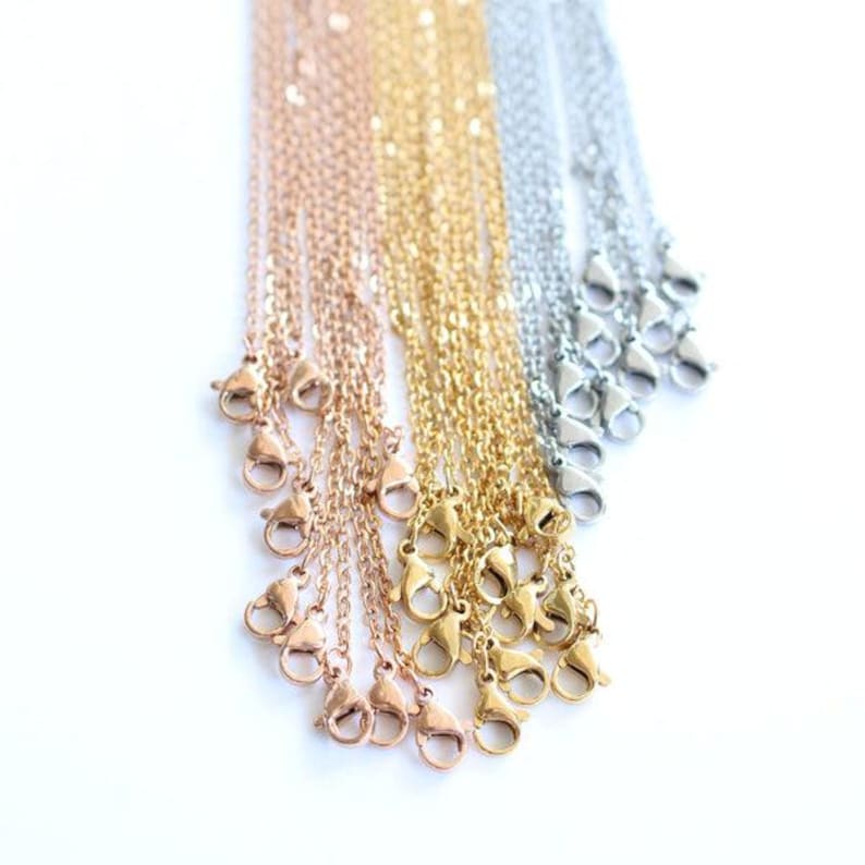 May include: An assortment of delicate chain necklaces in rose gold, gold, and silver tones. Each chain features a lobster clasp closure. The necklaces are displayed against a white background, showcasing their varying metallic finishes.