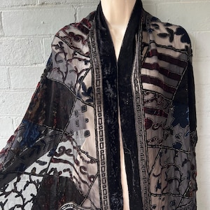 May include: A patchwork shawl with a black velvet collar and trim. The shawl features a variety of patterned fabrics in shades of black, gray, and burgundy. The design includes floral and geometric patterns.