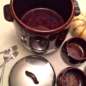 May include: A set of brown ceramic bowls with a silver lid. The bowls are all different sizes and have a glossy finish. The lid has a small handle.